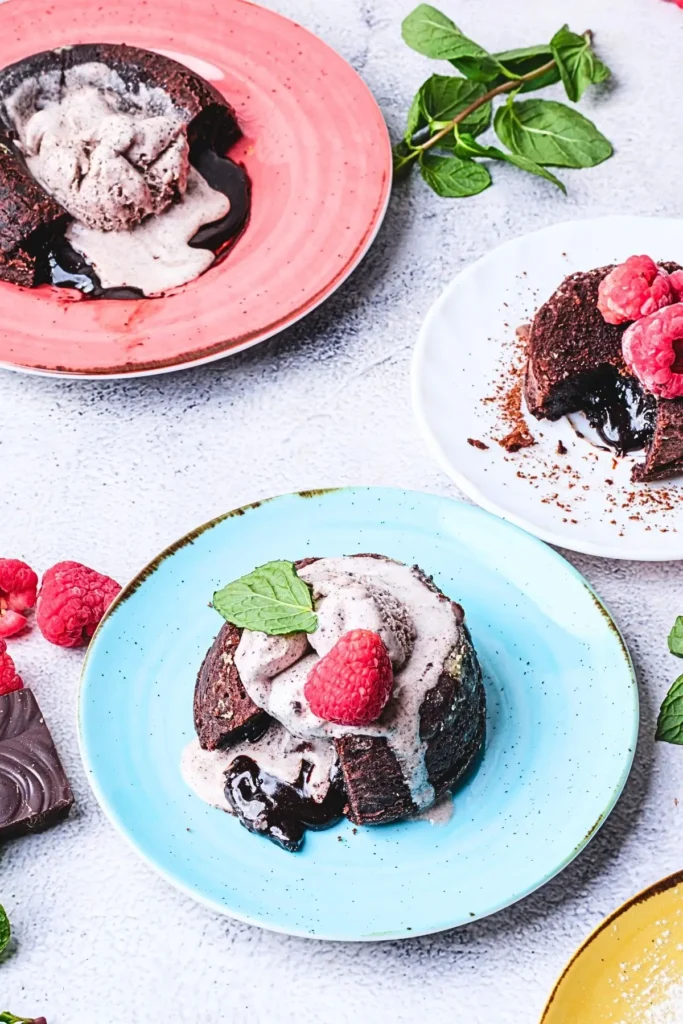 Molten lava chocolate cake on a blue plate, cut open with gooey chocolate, topped with whipped cream and a raspberry, garnished with mint leaves.