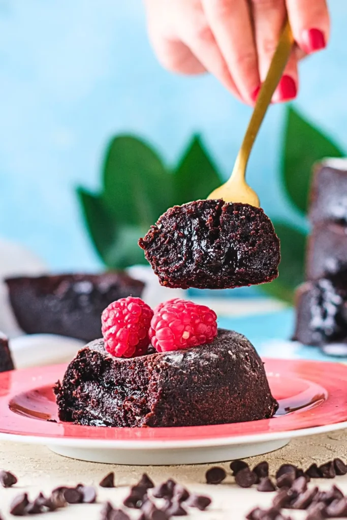 Molten lava chocolate cake on a white plate with three raspberries on top