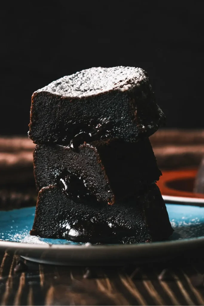 Stack of molten lava chocolate cakes on a blue plate, dusted with powdered sugar, showing gooey chocolate layers.