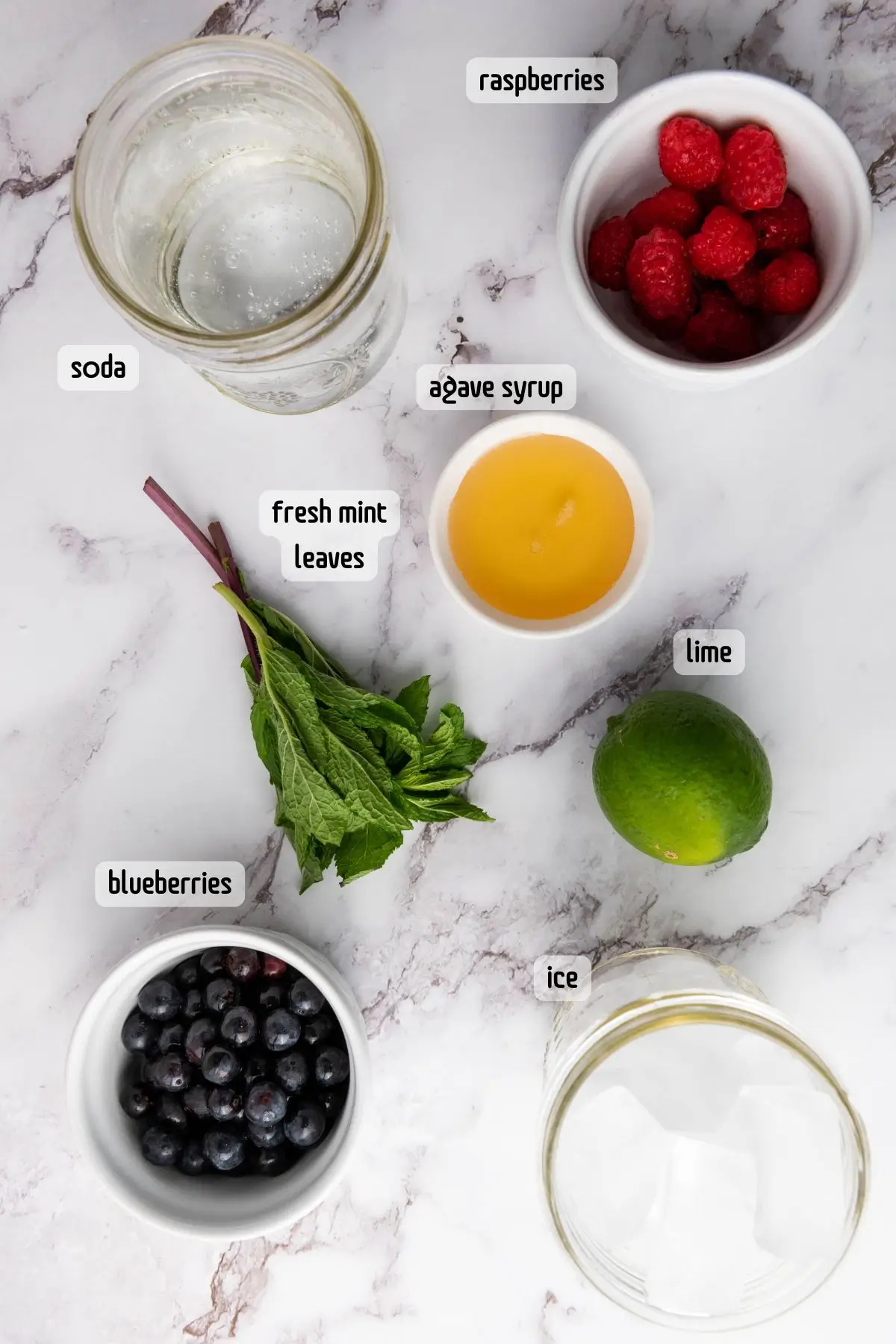ingredients on table with blueberries, raspberries, mint leaves, agave syrup, lime, and soda water for a blueberry raspberry mint mocktail, a yummy non alcoholic berry drink.