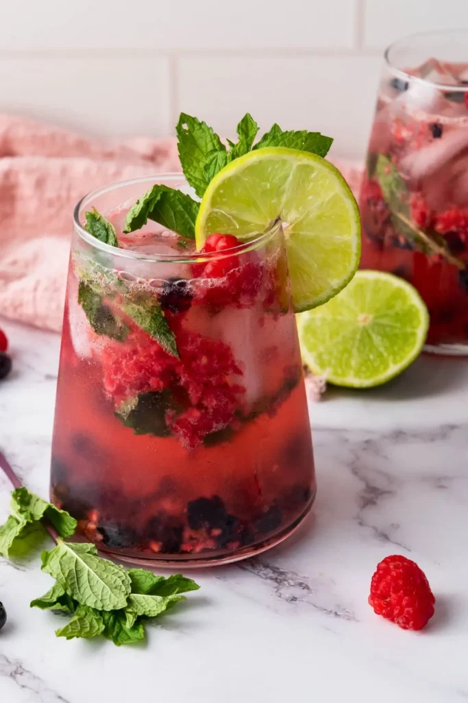 Close-up of a blueberry raspberry mint mocktail with a mint sprig and lime wedge on top, a tasty non alcoholic berry drink for summer parties.