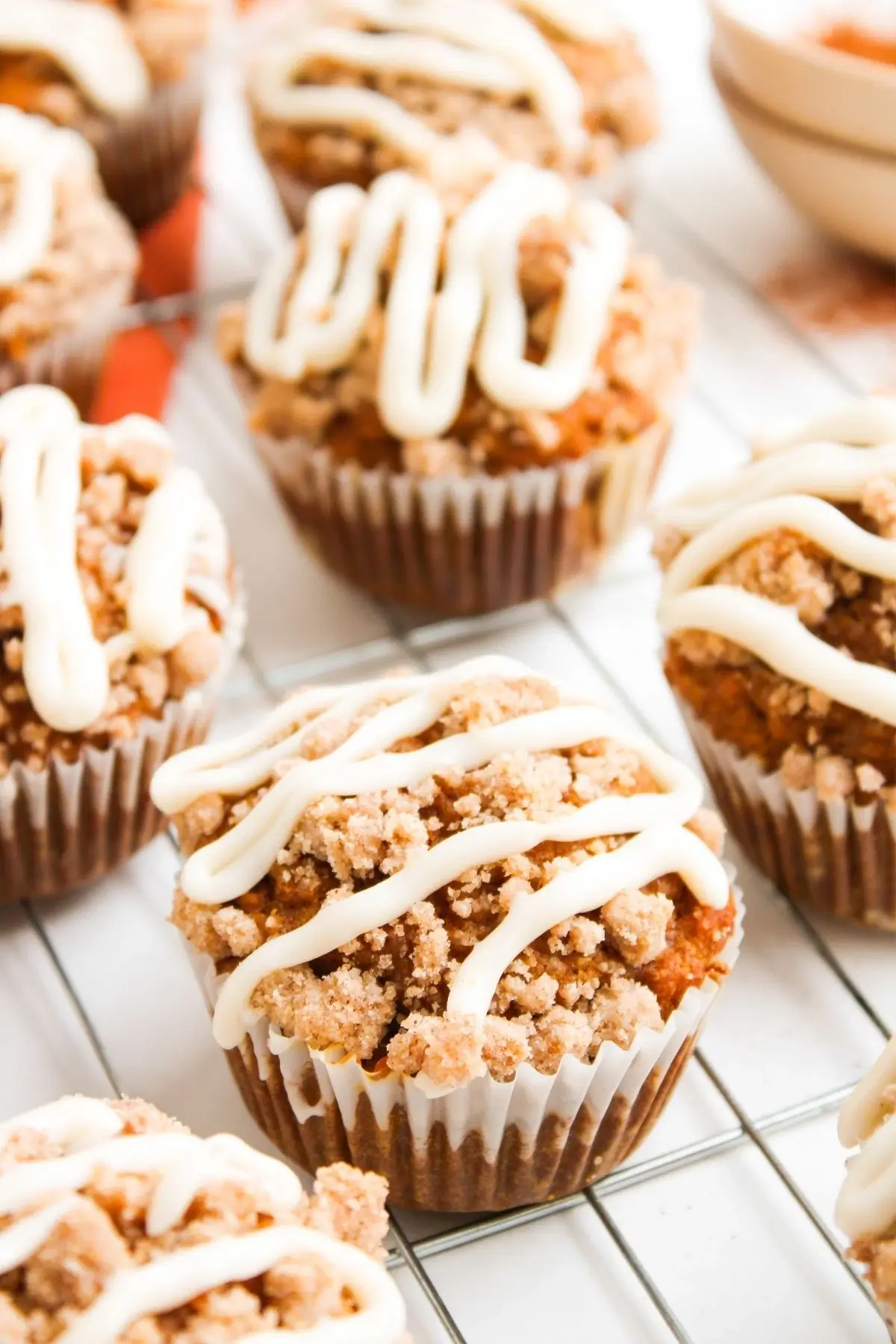 Close-up view of baked pumpkin muffins topped with streusel and thick cream cheese drizzle on a cooling rack.