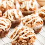 Multiple pumpkin muffins with streusel topping and cream cheese drizzle cooling on a wire rack.