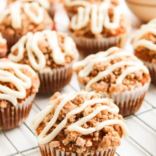 Multiple pumpkin muffins with streusel topping and cream cheese drizzle cooling on a wire rack.