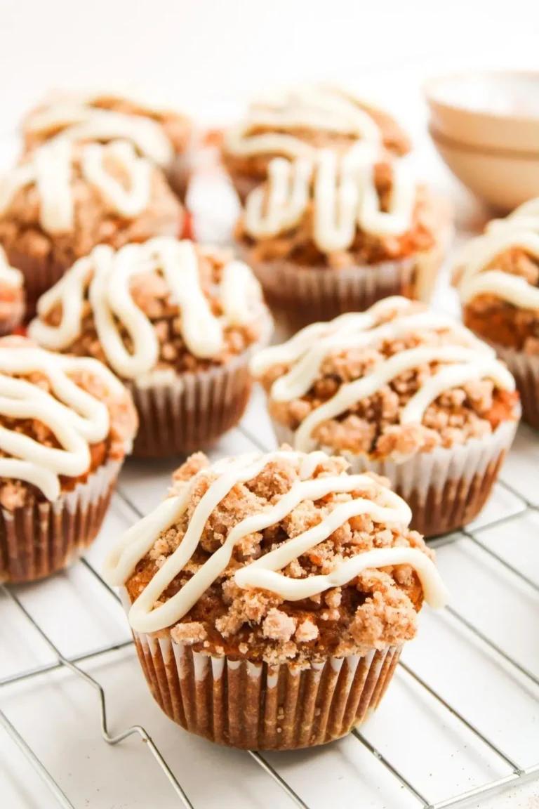 Multiple pumpkin muffins with streusel topping and cream cheese drizzle cooling on a wire rack.