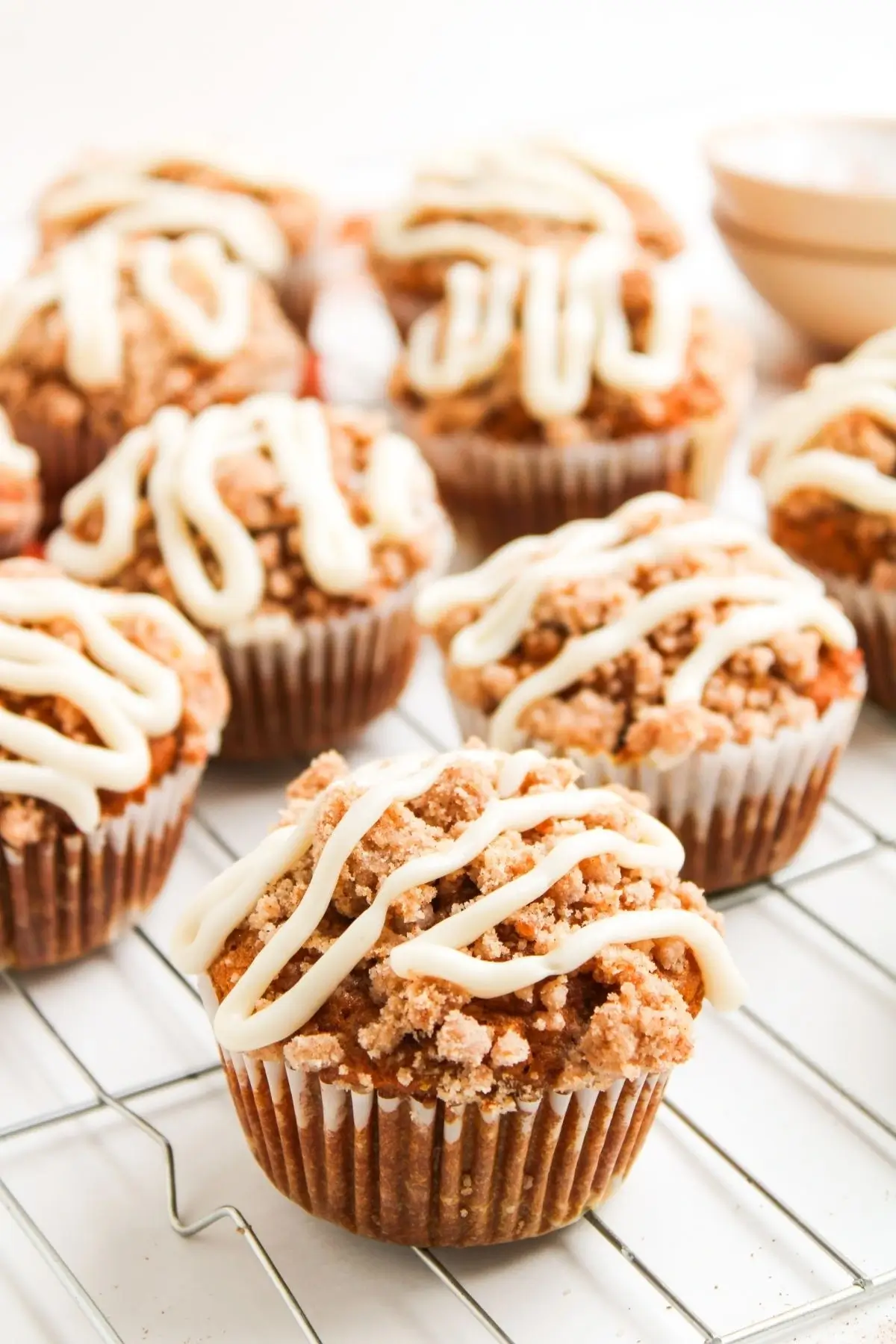 Multiple pumpkin muffins with streusel topping and cream cheese drizzle cooling on a wire rack.