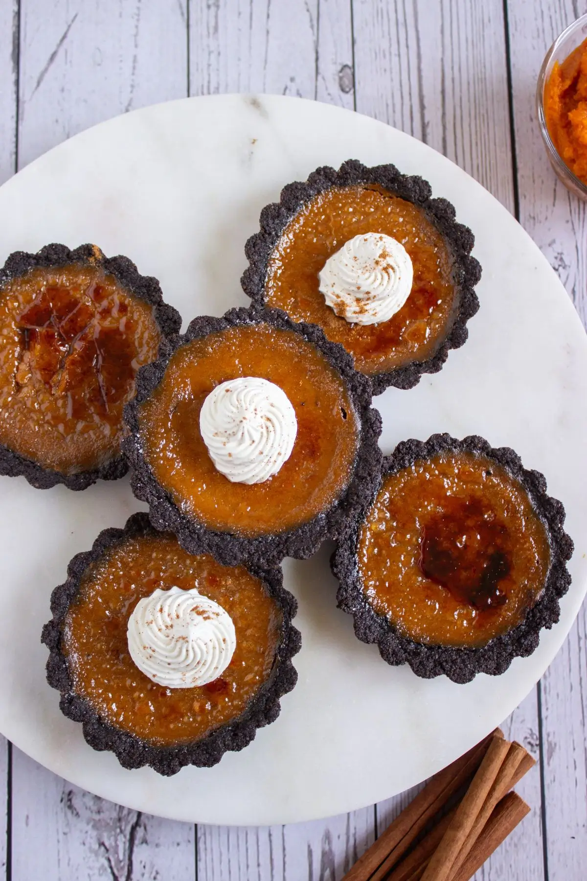 Beautiful pumpkin creme brulee tartlets with whipped cream topping, golden caramelized sugar, and chocolate crust.