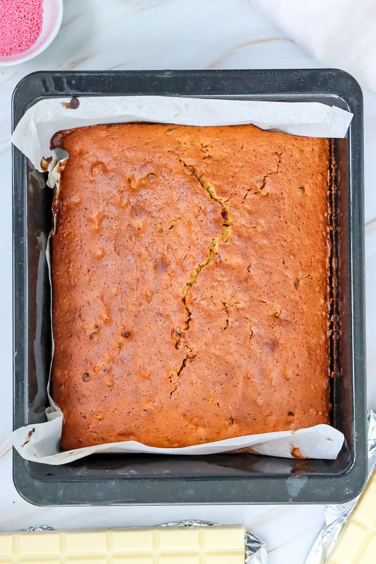 Golden-brown tray bake cake cooling in a parchment-lined pan.