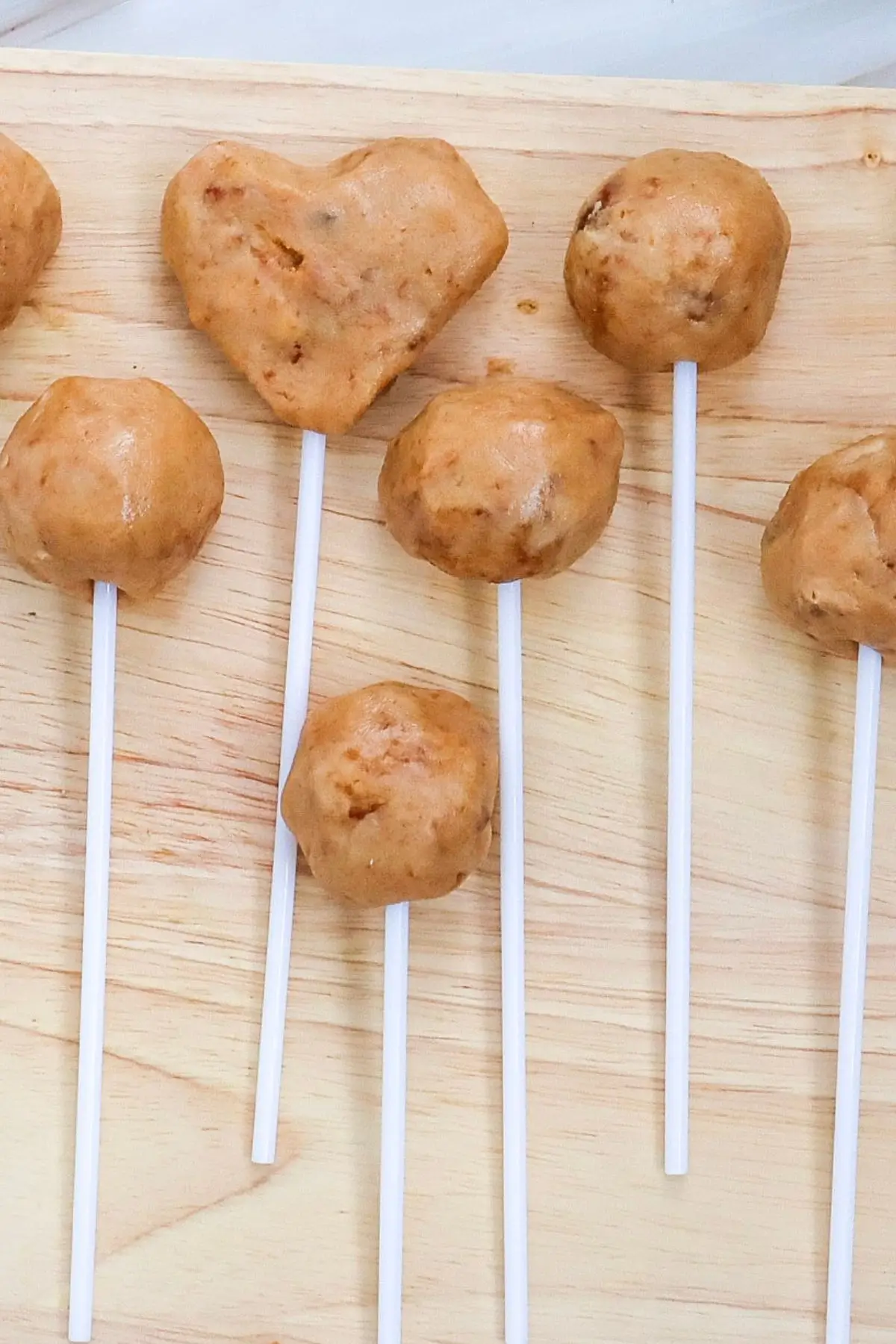 Homemade undipped cake pops, including a heart shape, on sticks over wooden board