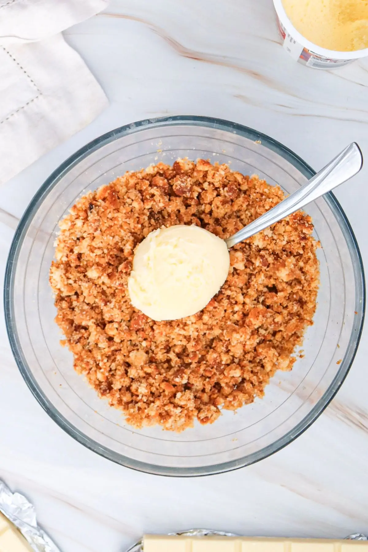 Glass bowl of crushed cookie crumbs with a spoonful of melted butter for cheesecake crust prep
