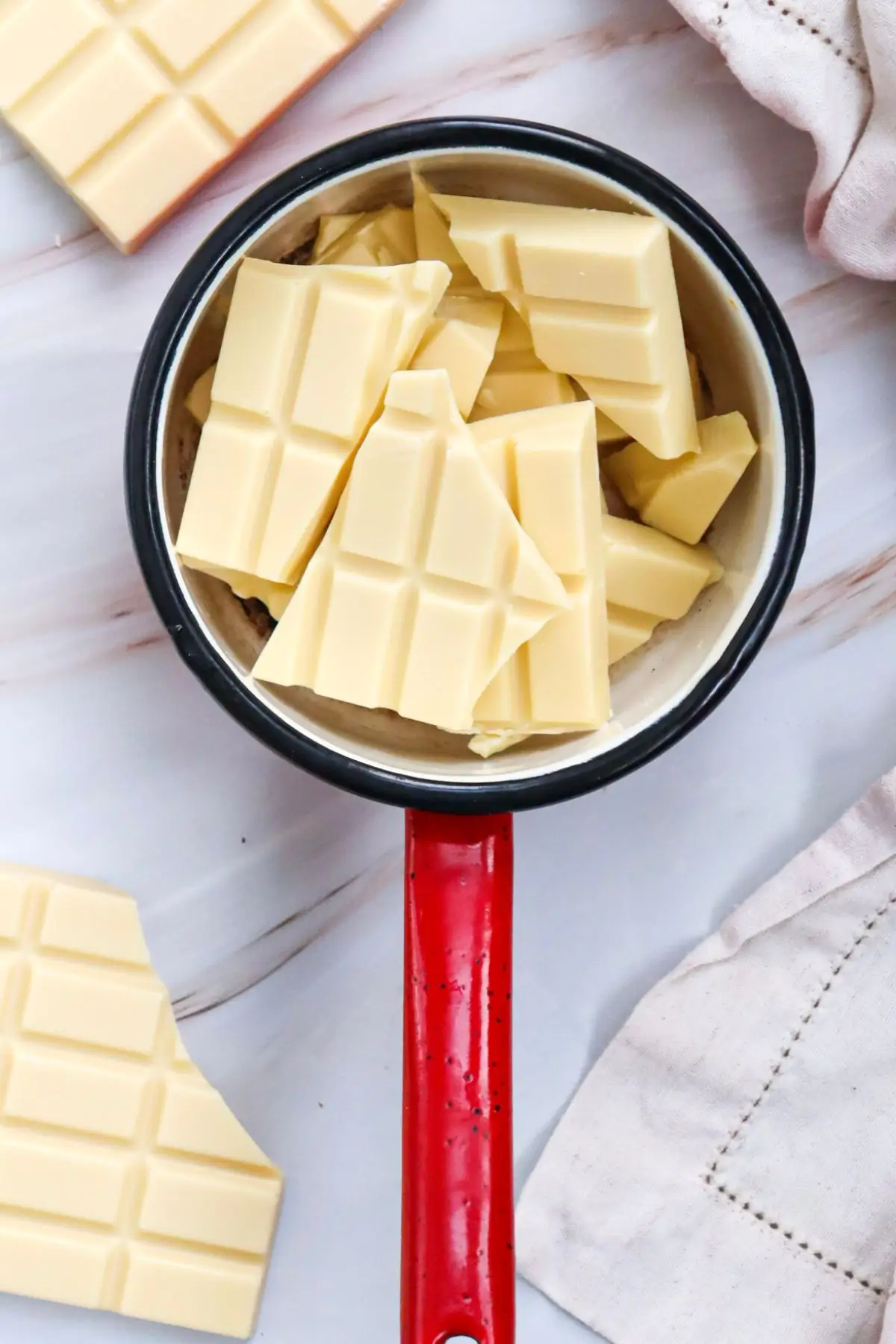 White chocolate chunks in a small saucepan with red handle, ready for melting