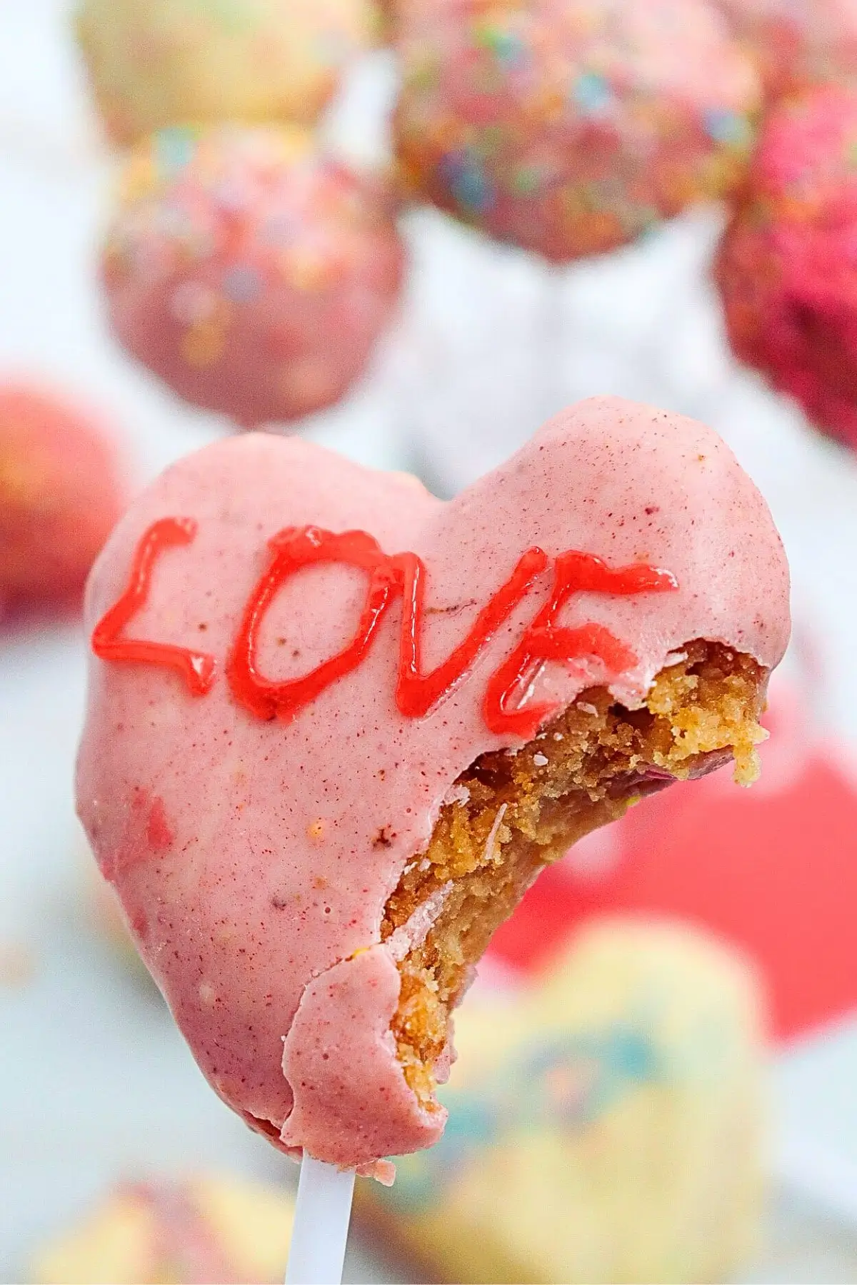 Bite taken from heart-shaped pink cake pop with LOVE icing, a cute Valentine treat