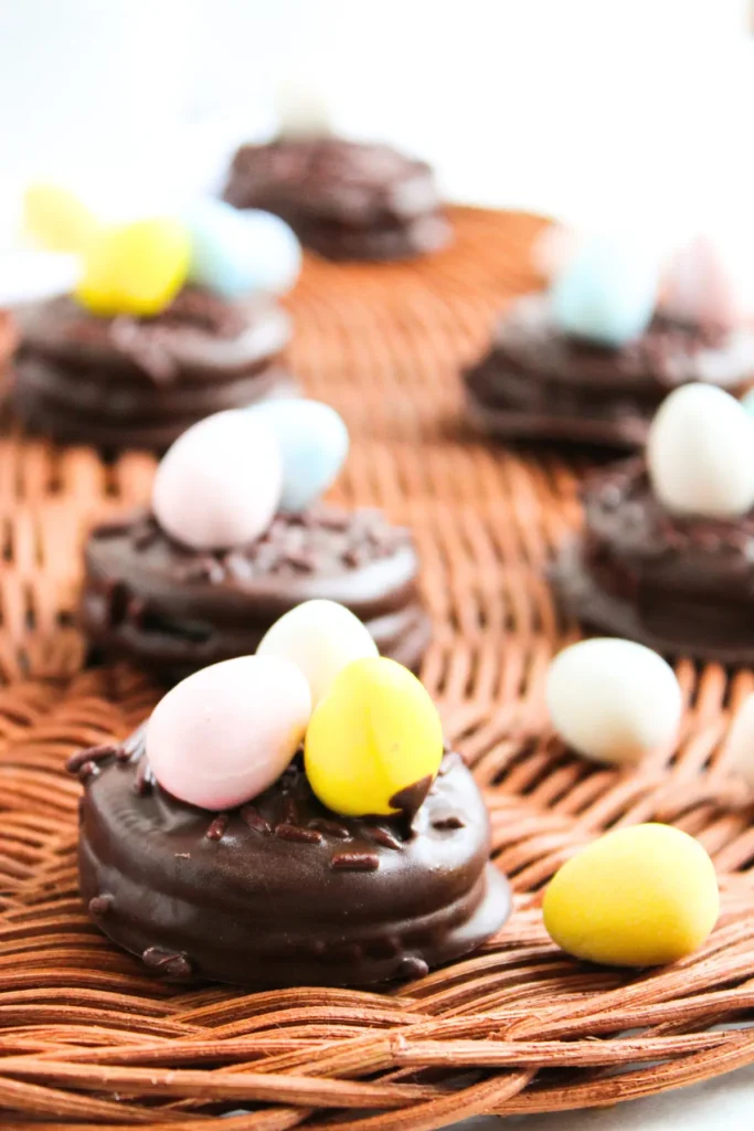 Easter chocolate-covered cookie nests topped with pastel candy eggs on a woven tray