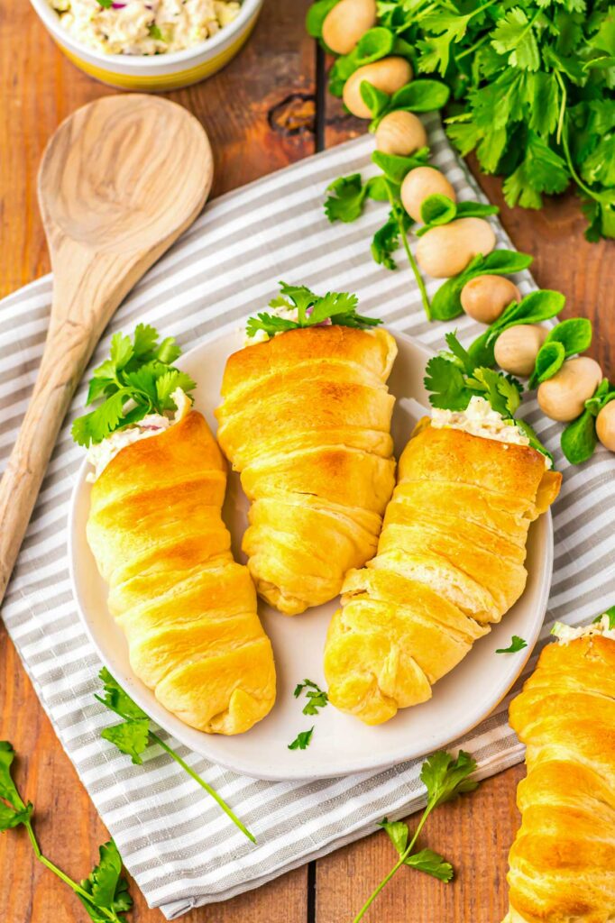 Golden crescent roll cones filled with creamy chicken salad and fresh herbs on a white plate