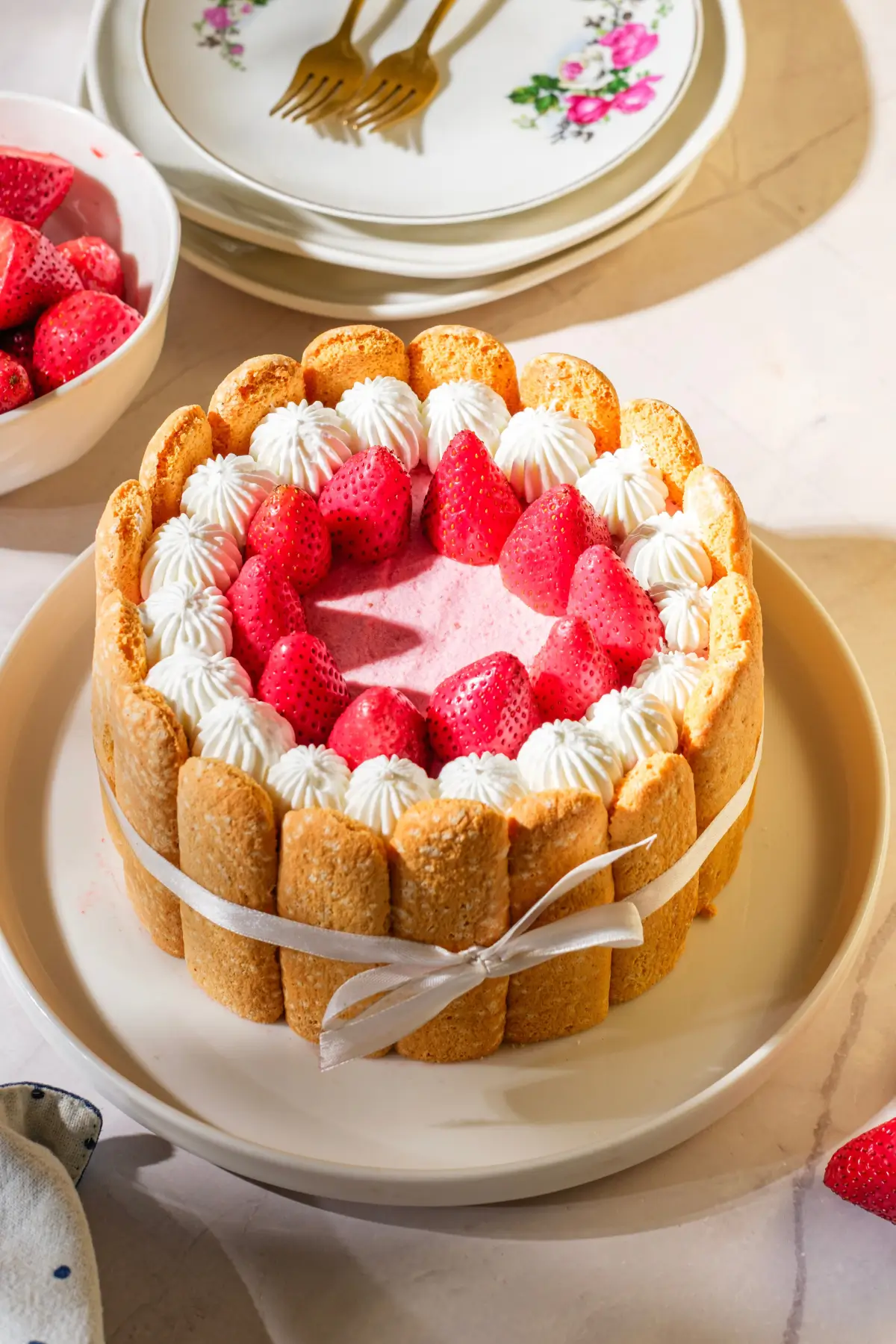 Strawberry Charlotte Cake Strawberry charlotte cake with ladyfingers, whipped cream, and fresh berries, tied with ribbon on a white plate