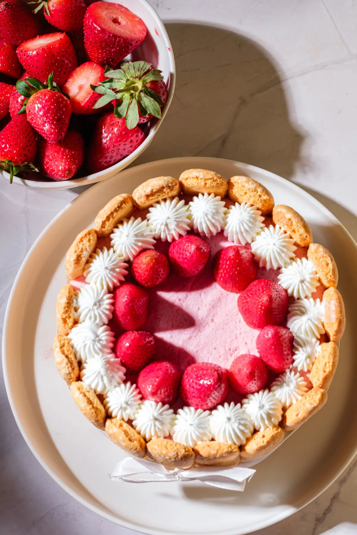 Strawberry charlotte cake with ladyfingers, whipped cream, and fresh berries on a plate.