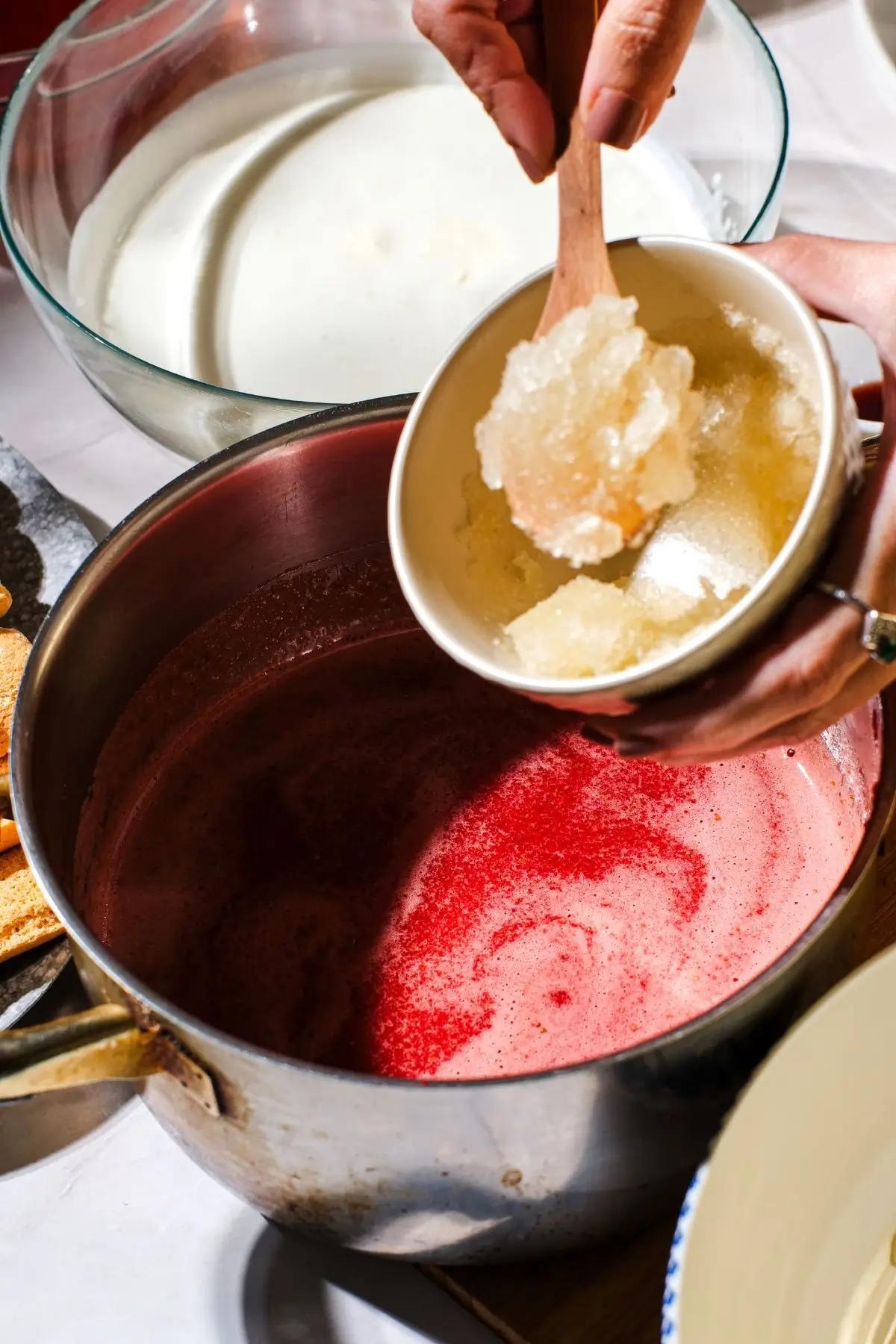 Hand adding bloomed gelatin to raspberry puree in a stainless pot for mousse