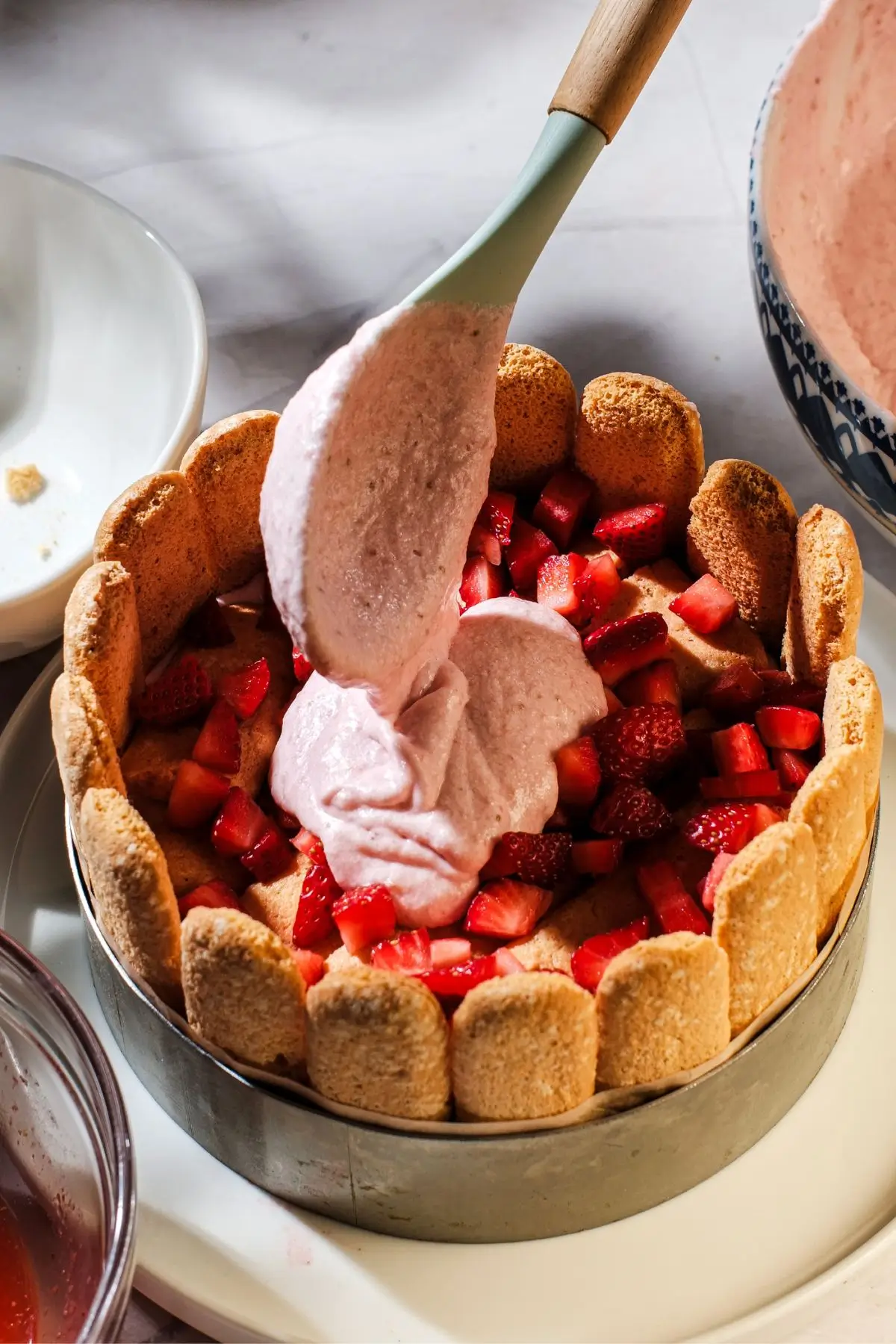 Spoon adding strawberry mousse to a ladyfinger charlotte filled with fresh berries