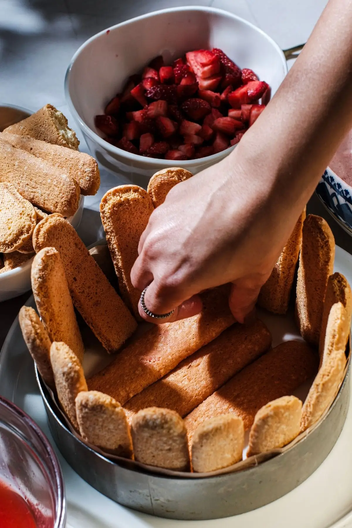 Close-up of a hand lining ladyfingers in a springform pan for a strawberry charlotte
