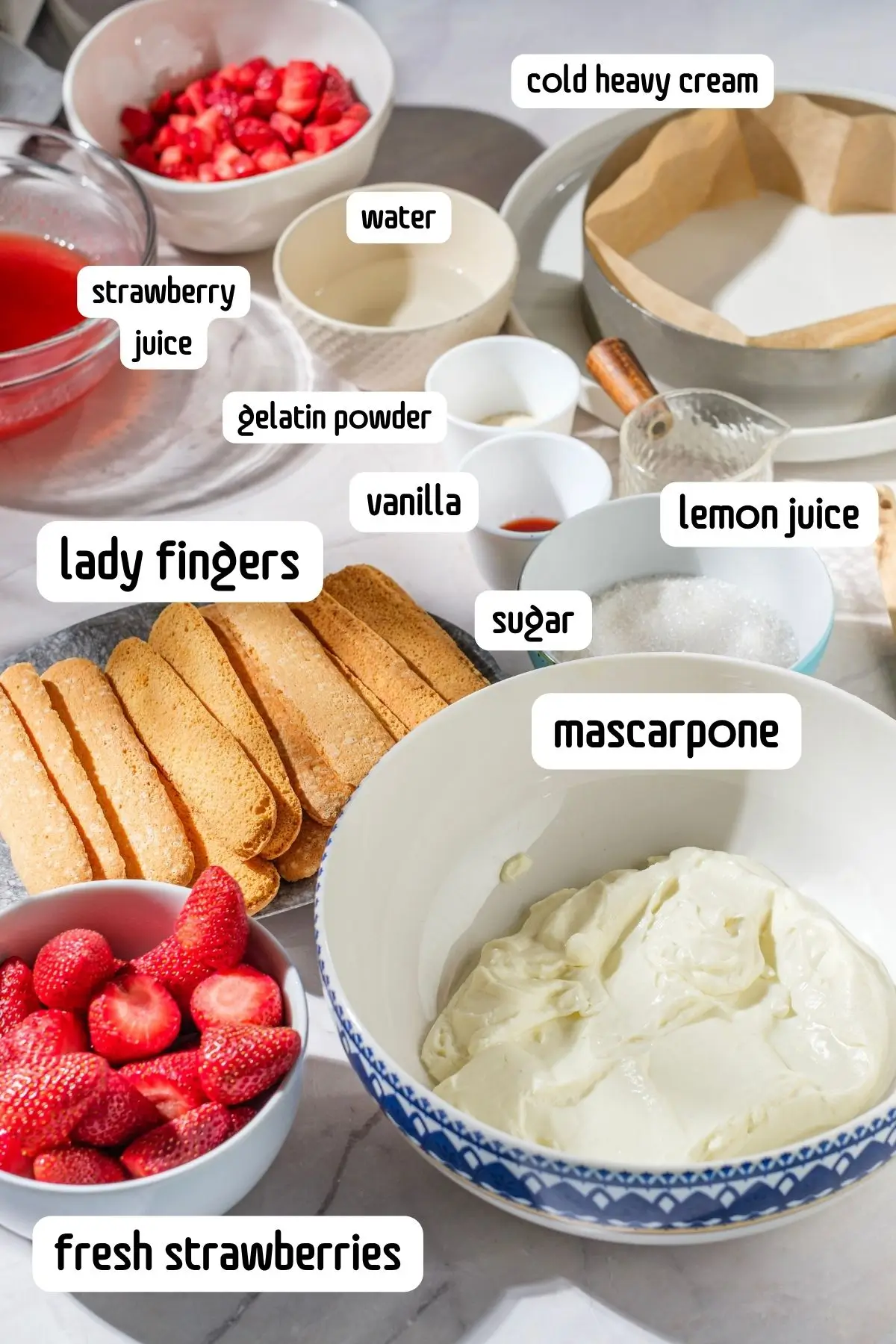 Overhead shot of ingredients for strawberry mascarpone dessert: ladyfingers, fresh strawberries, gelatin, sugar, lemon, cream