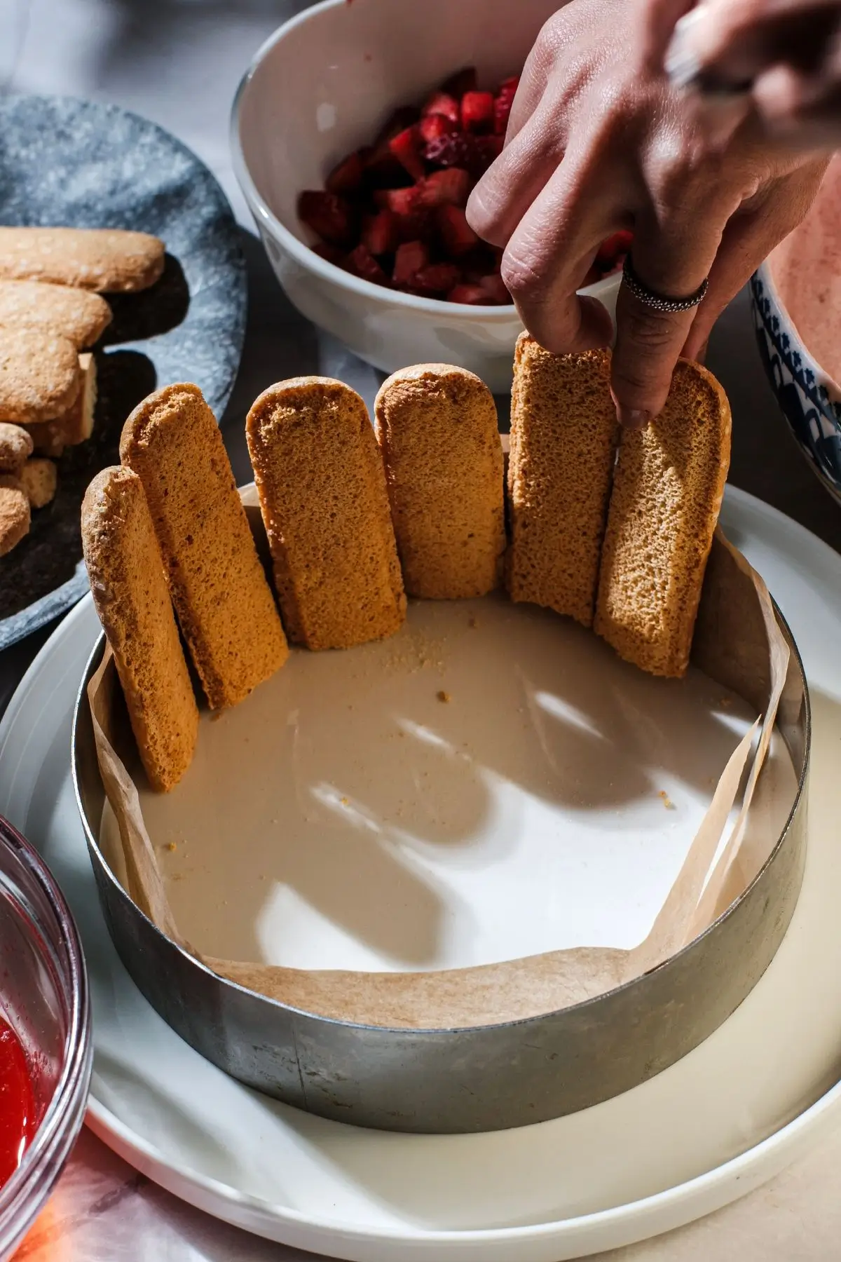 Hand lining a cake ring with ladyfinger biscuits for a strawberry charlotte or tiramisu dessert