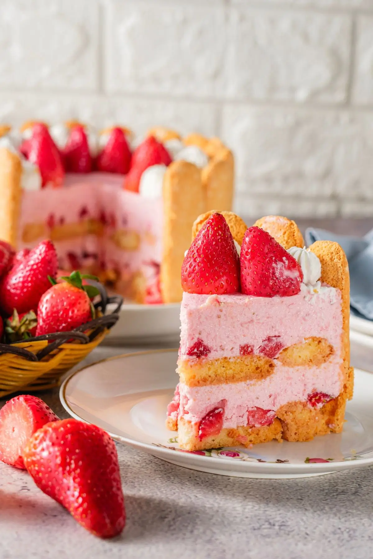Slice of strawberry charlotte cake with ladyfingers, mousse filling, and fresh strawberries on top