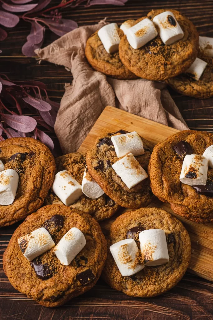Homemade s'mores cookies with toasted marshmallows and dark chocolate on a rustic wooden board