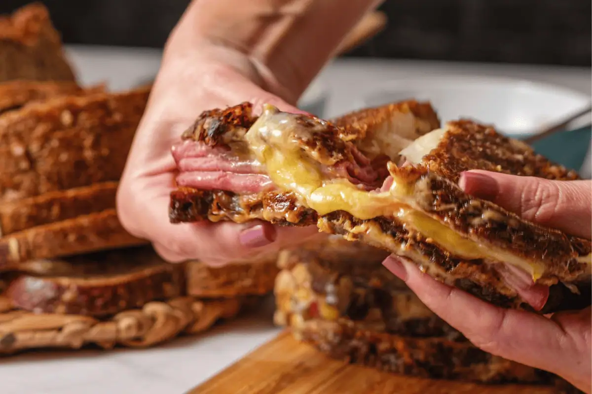 Hands pulling apart a hot ham and melted cheese grilled sandwich on rustic bread