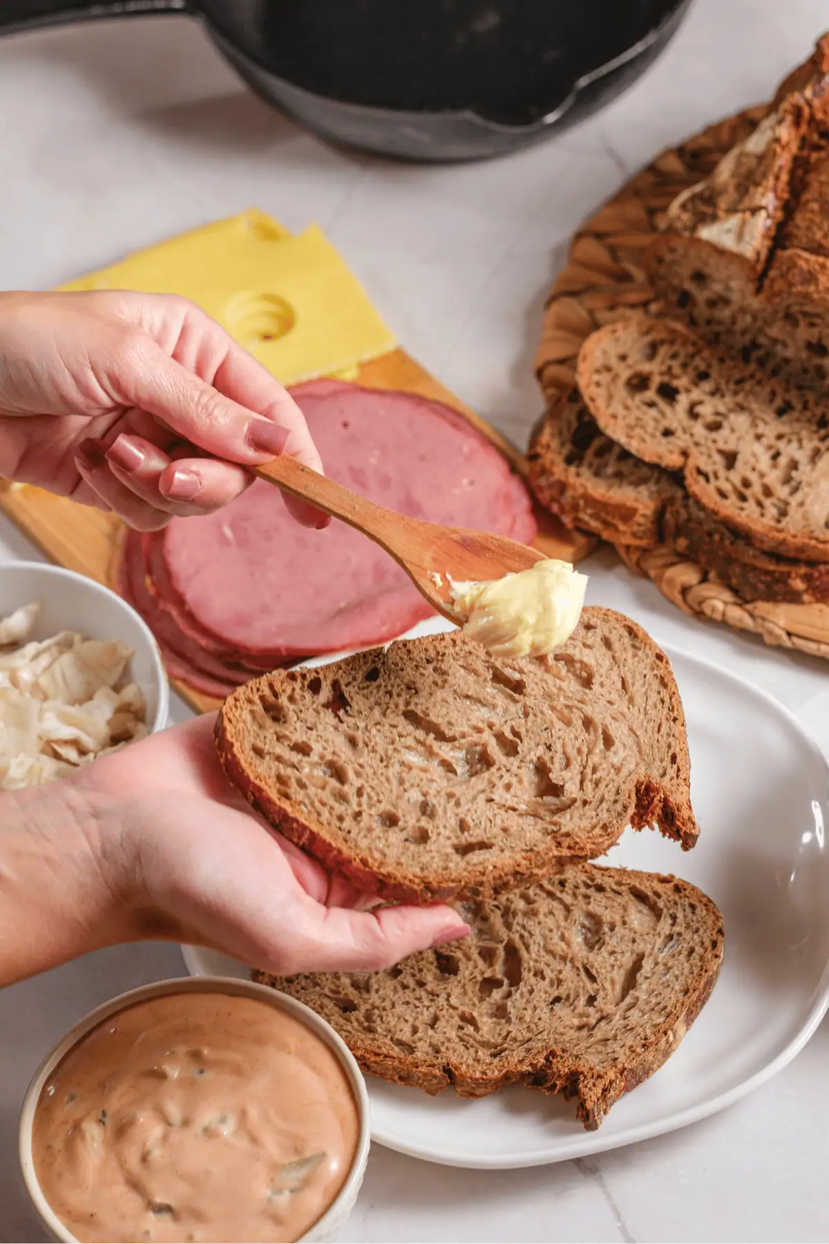 Spreading butter on rye bread for homemade Reuben sandwich with corned beef, Swiss, kraut, and dressing