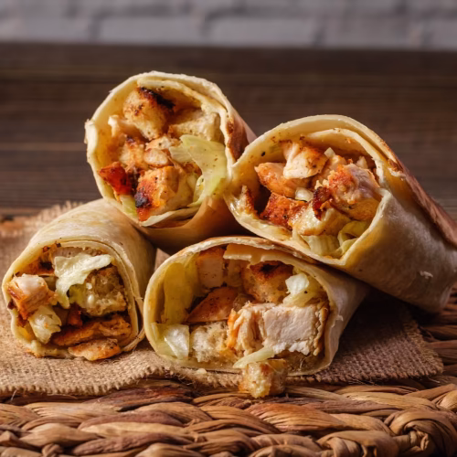Crispy chicken Caesar wraps with croutons, grilled chicken, lettuce, and creamy dressing sliced open on a rustic wooden table.