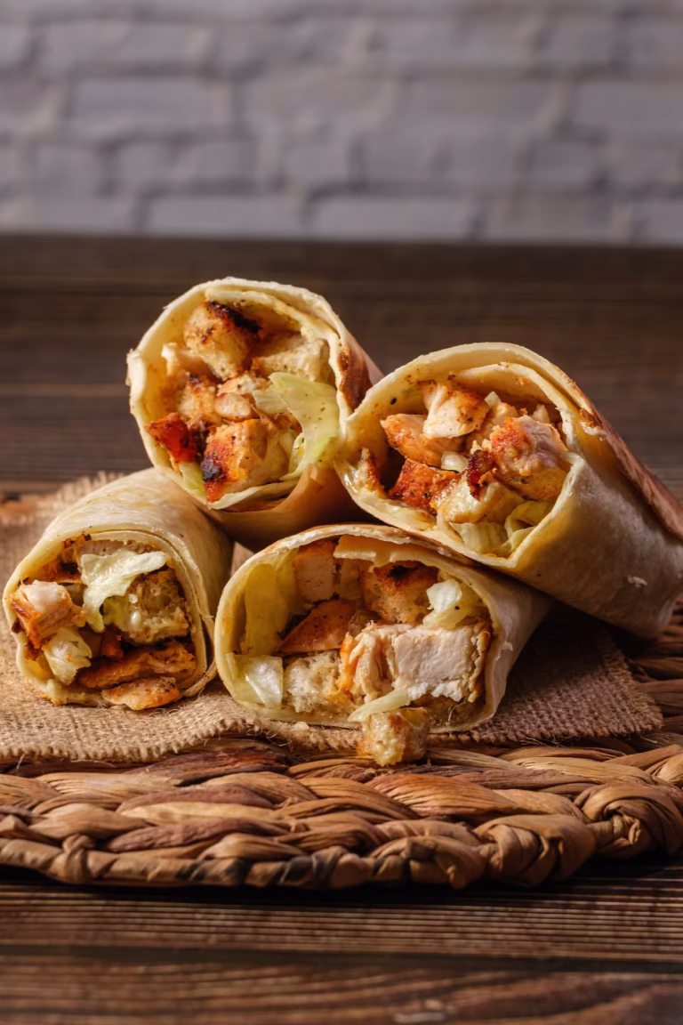 Crispy chicken Caesar wraps with croutons, grilled chicken, lettuce, and creamy dressing sliced open on a rustic wooden table.