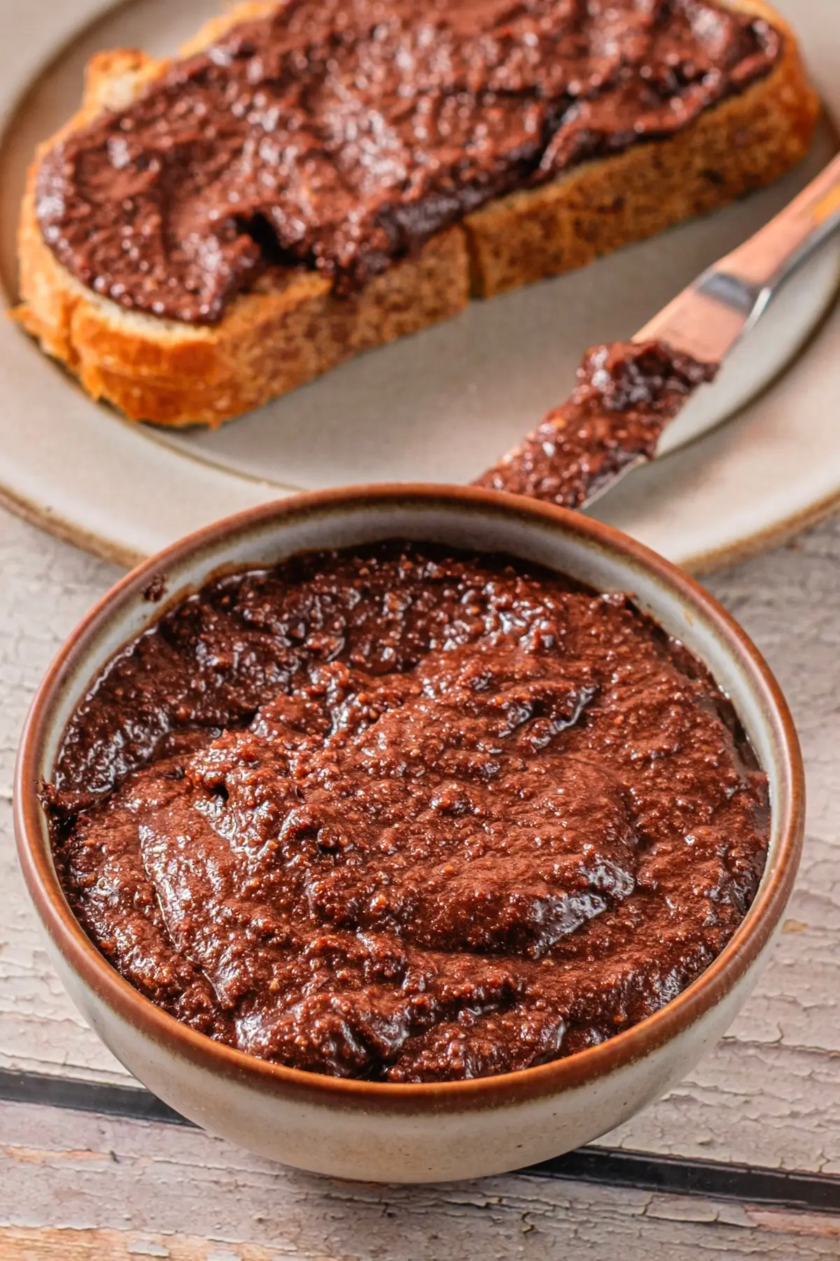 Bowl of homemade chocolate hazelnut spread with knife and slice of toast on plate
