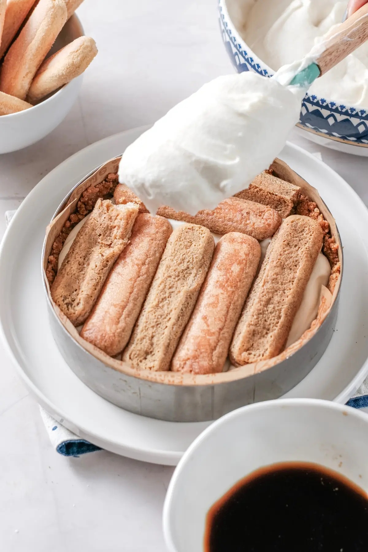 Layering mascarpone cream over espresso-soaked ladyfingers for homemade tiramisu cheesecake