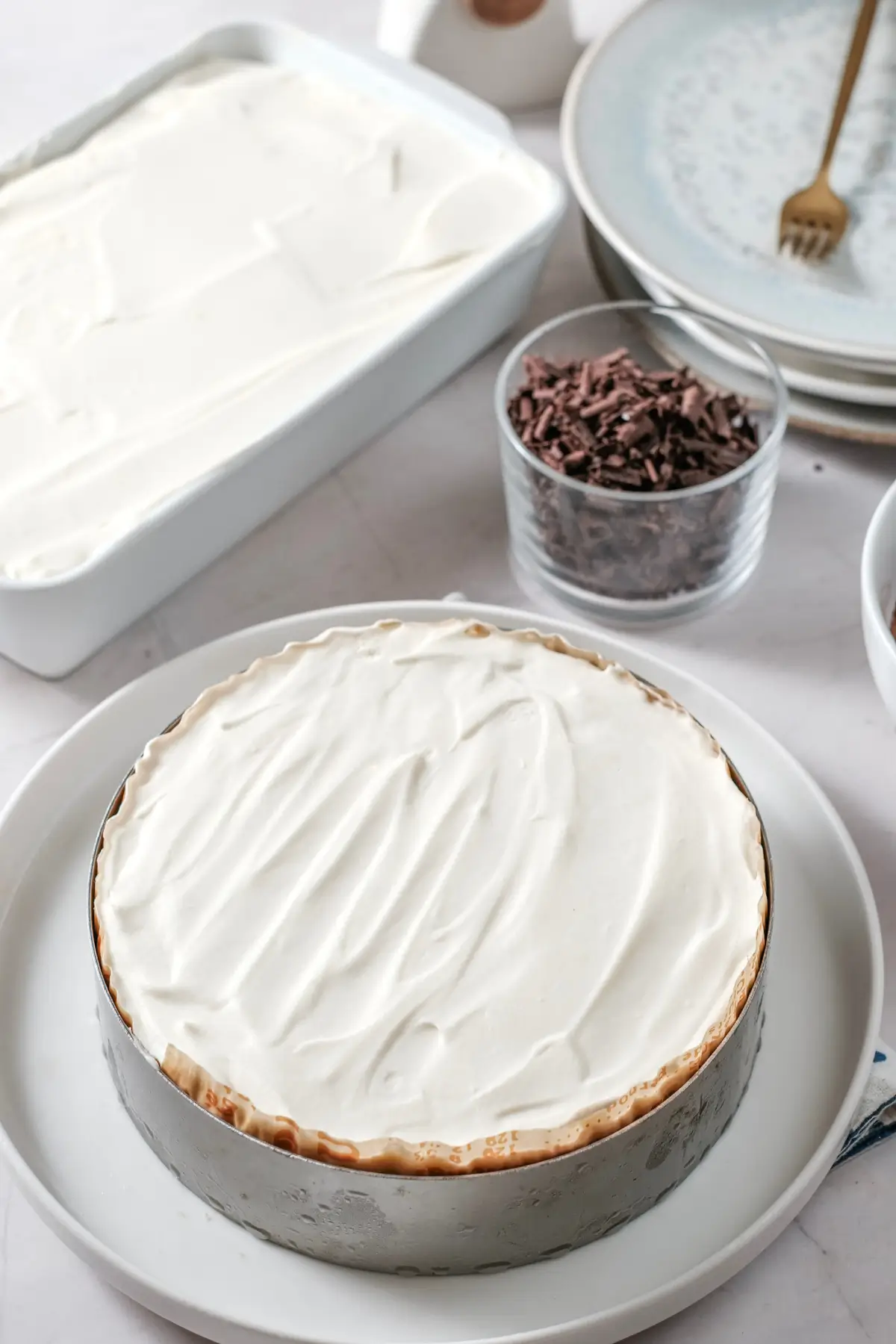 No-bake dessert with whipped cream in a springform pan, with chocolate shavings and serving plates