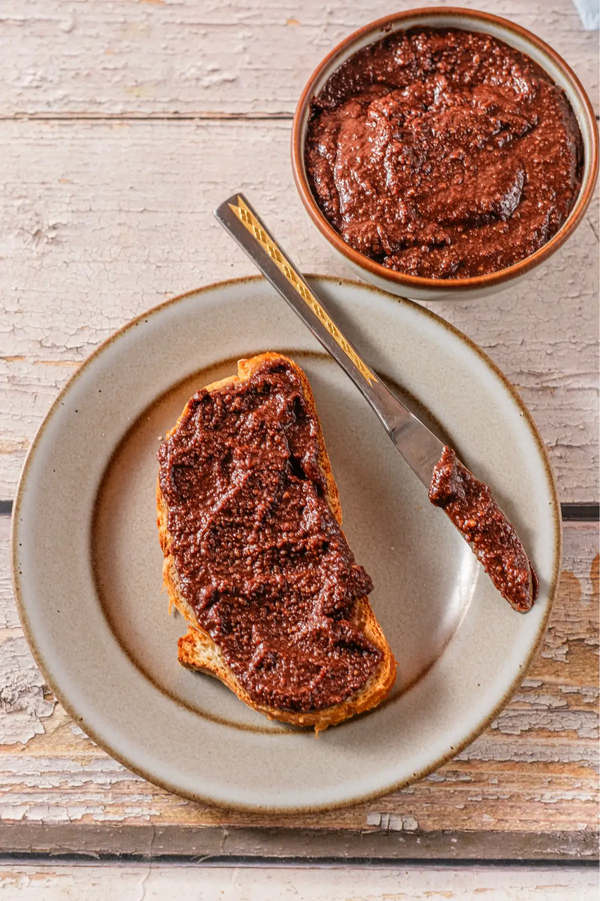 Toast with chocolate spread on a plate, butter knife and bowl on a rustic wooden table