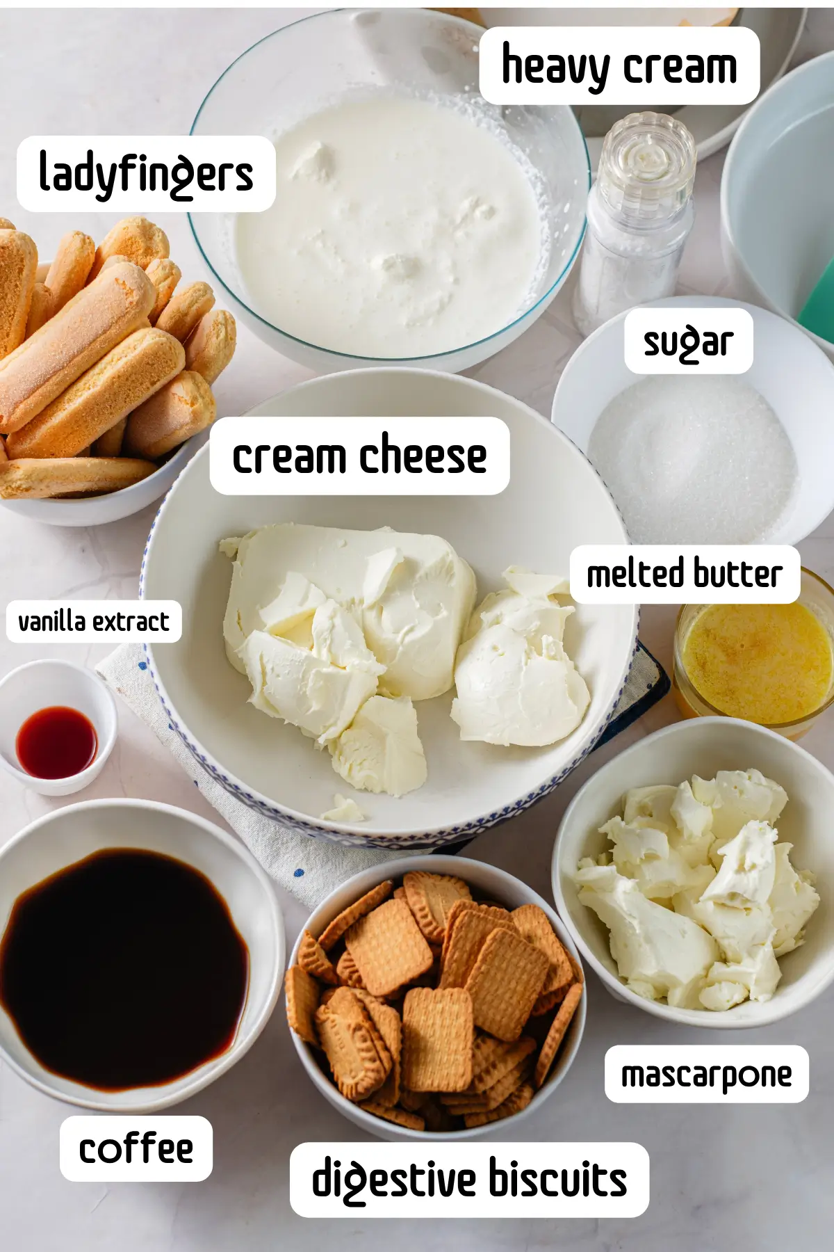 Flat lay of tiramisu cheesecake ingredients: ladyfingers, mascarpone, cream cheese, coffee, heavy cream, sugar, butter.