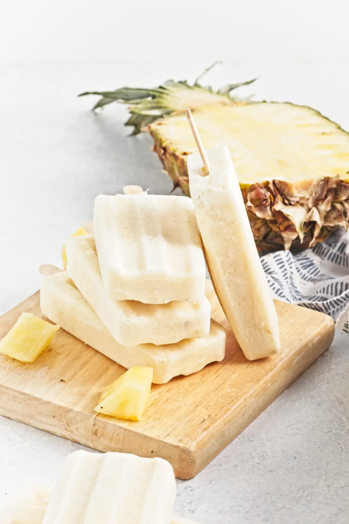 Creamy pina colada popsicles stacked on a wooden board with pineapple