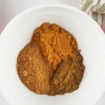 Ground cinnamon, nutmeg, and cloves added to a white mixing bowl.
