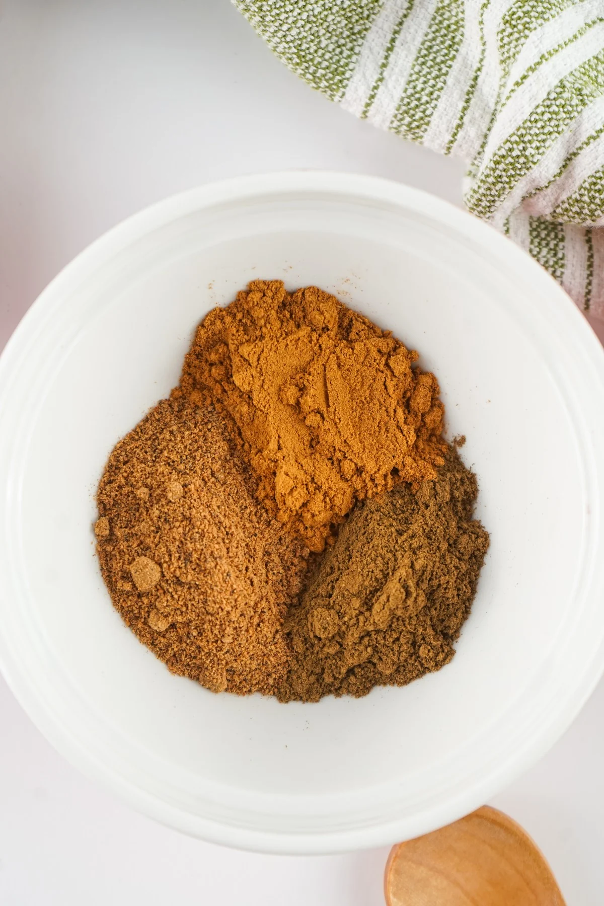 Ground cinnamon, nutmeg, and cloves added to a white mixing bowl.