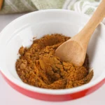A wooden spoon stirring the homemade allspice substitute in a bowl.
