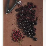 Pitted and chopped cherries on a cutting board with a cherry pitter.