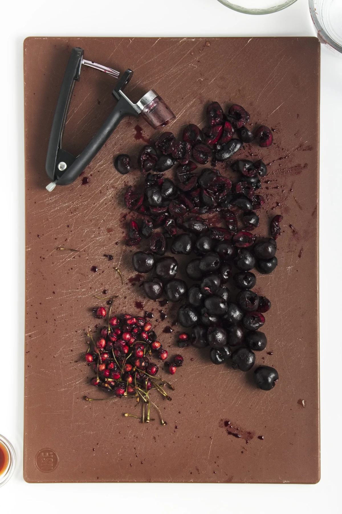 Pitted and chopped cherries on a cutting board with a cherry pitter.