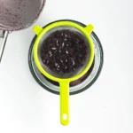 Cooked cherries being strained through a fine mesh sieve to make cherry syrup.