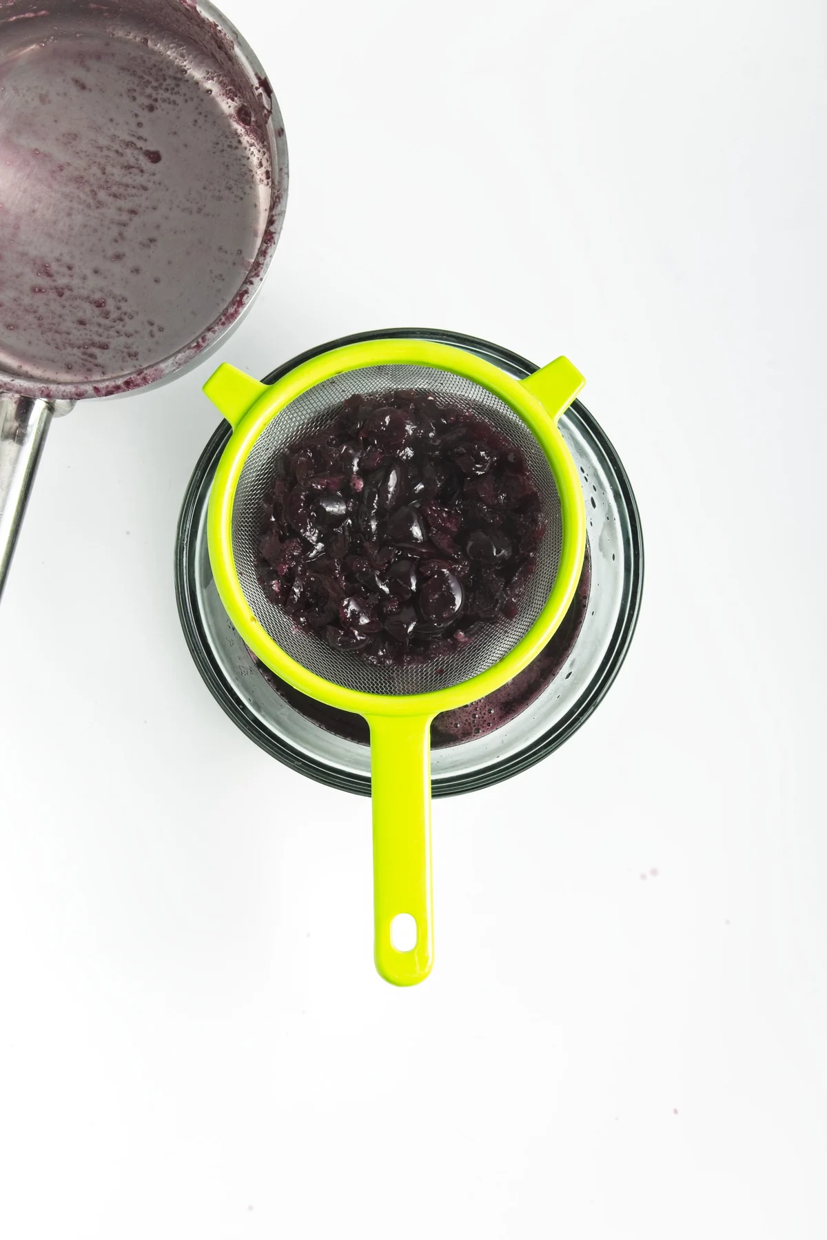 Cooked cherries being strained through a fine mesh sieve to make cherry syrup.