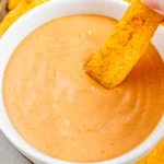 A seasoned fry being dipped into creamy campfire sauce.