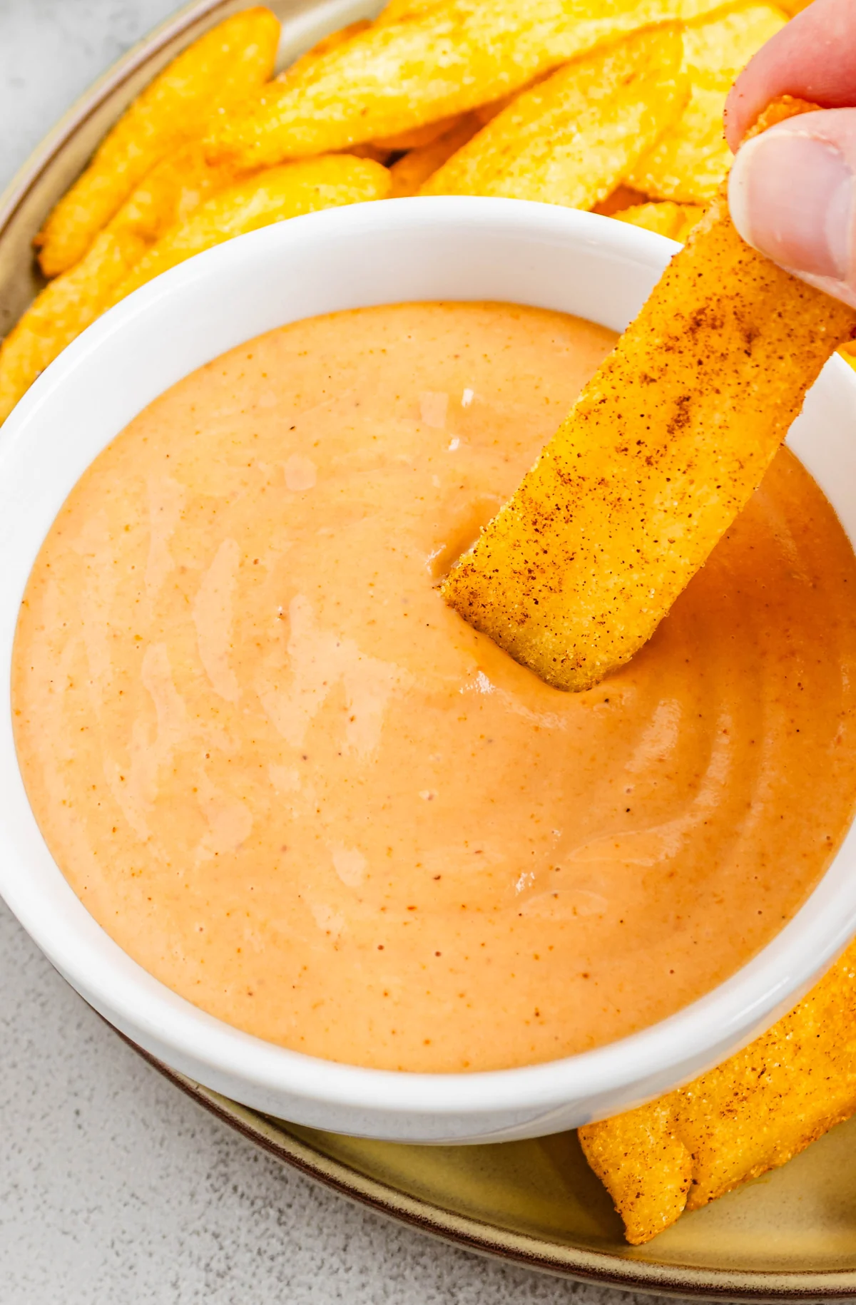 A seasoned fry being dipped into creamy campfire sauce.