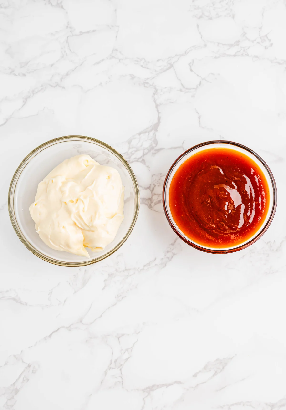 Mayonnaise and whiskey BBQ sauce in glass bowls on a marble surface.