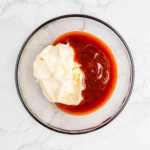 Mayonnaise and BBQ sauce added to a glass mixing bowl for campfire sauce.