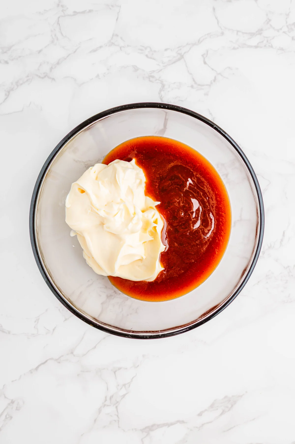 Mayonnaise and BBQ sauce added to a glass mixing bowl for campfire sauce.