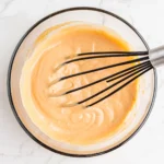 Smooth orange campfire sauce mixed in a glass bowl with a whisk.